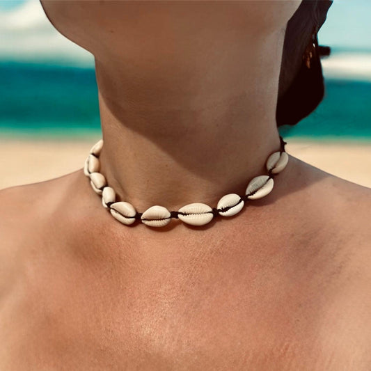 Woman wearing cowrie shell necklace on a beach.