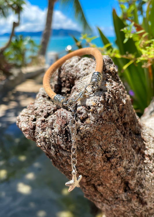 cork bracelet with engraved silver fittings, chain and starfish pendant - displayed on a rock with beach and sea behind - Ben's Beach Jewellery