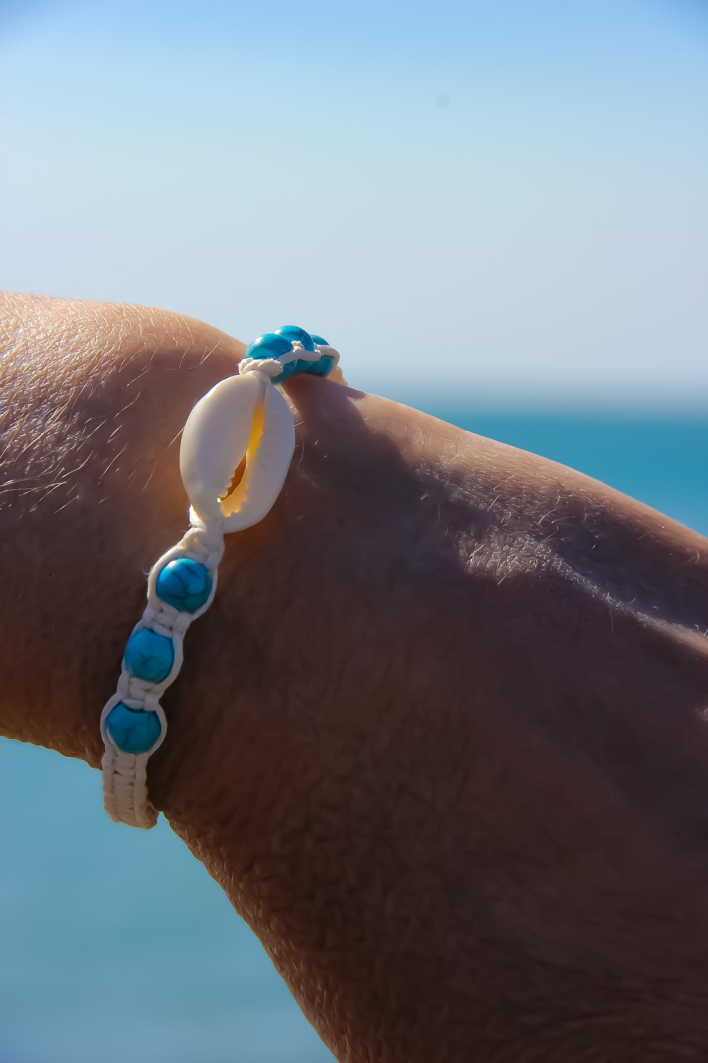 Cream braided bracelet on a model's hand. Bracelet has a cowrie shell pendant and blue stone beads. 