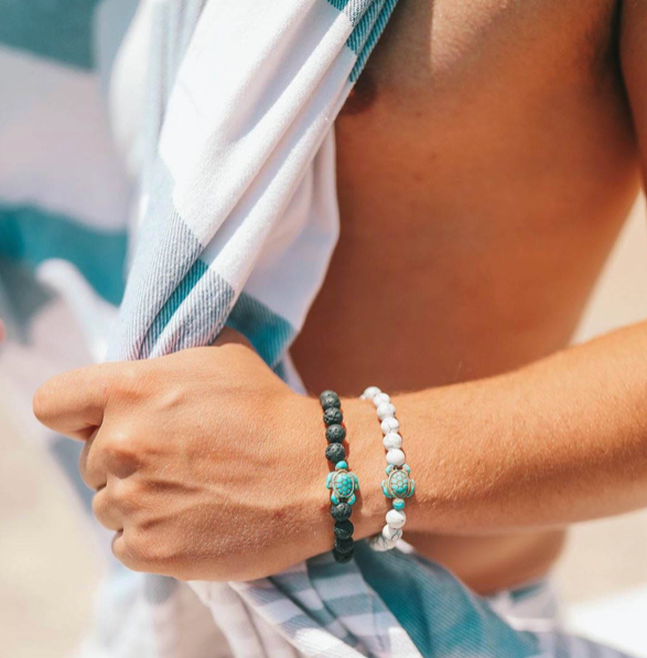 Male model with beach towel and wearing stone bead beach bracelets with turtle pendants