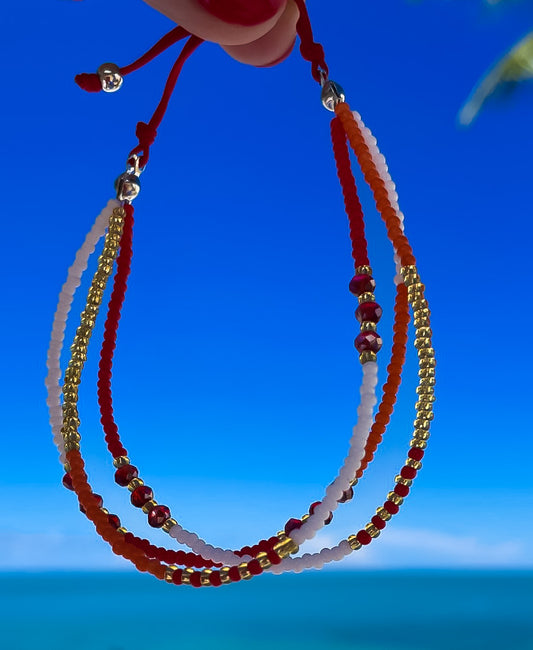 Red and white seed bead anklet held against a blue sky