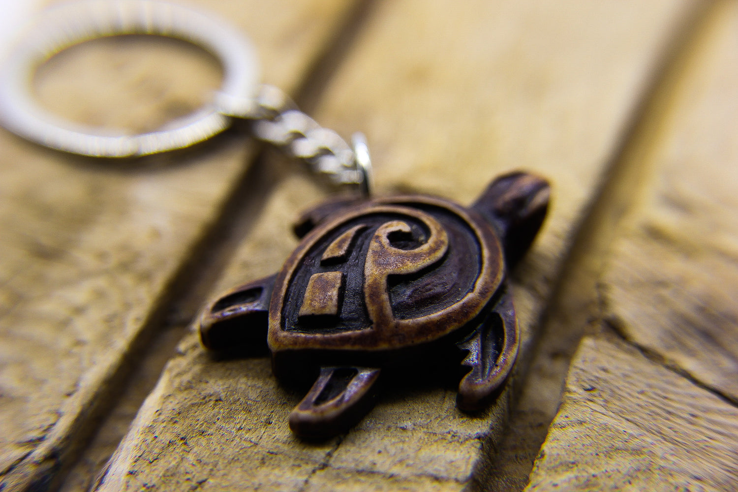 Carved Hawaiian style sea turtle pendant key ring on a piece of wood.  