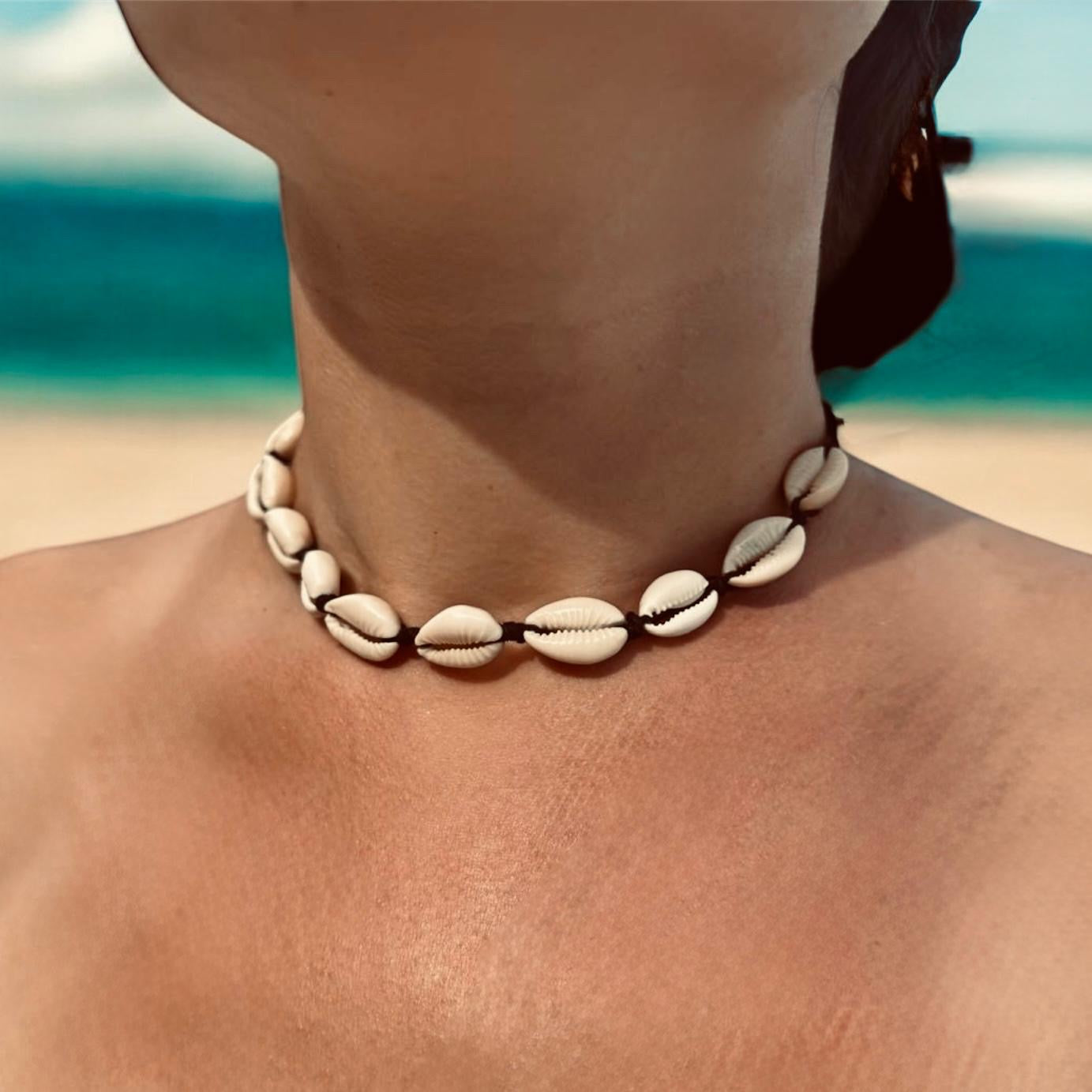 Woman wearing cowrie shell necklace on a beach. 