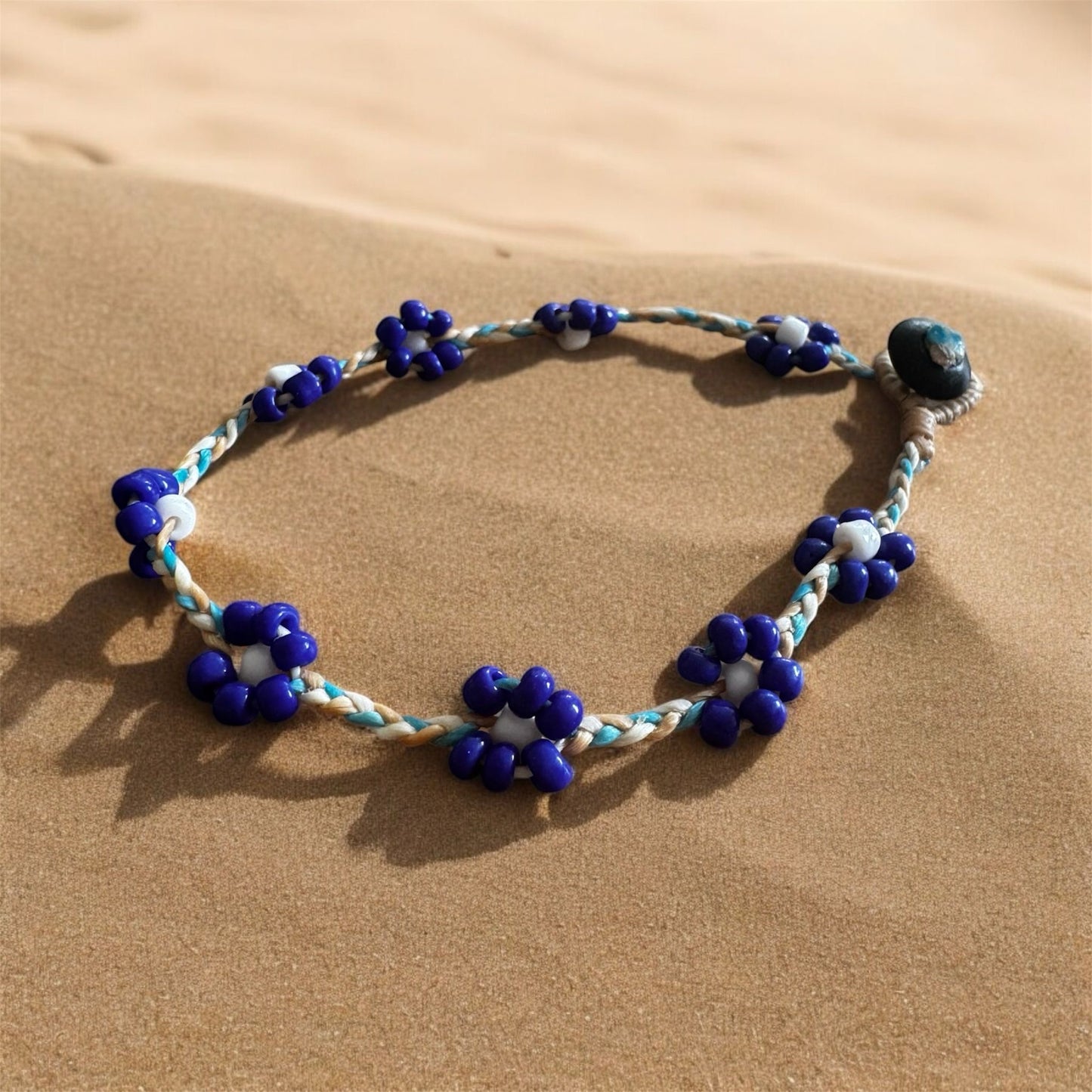 String anklet with beads in a flower design. Anklet is on a beach. 