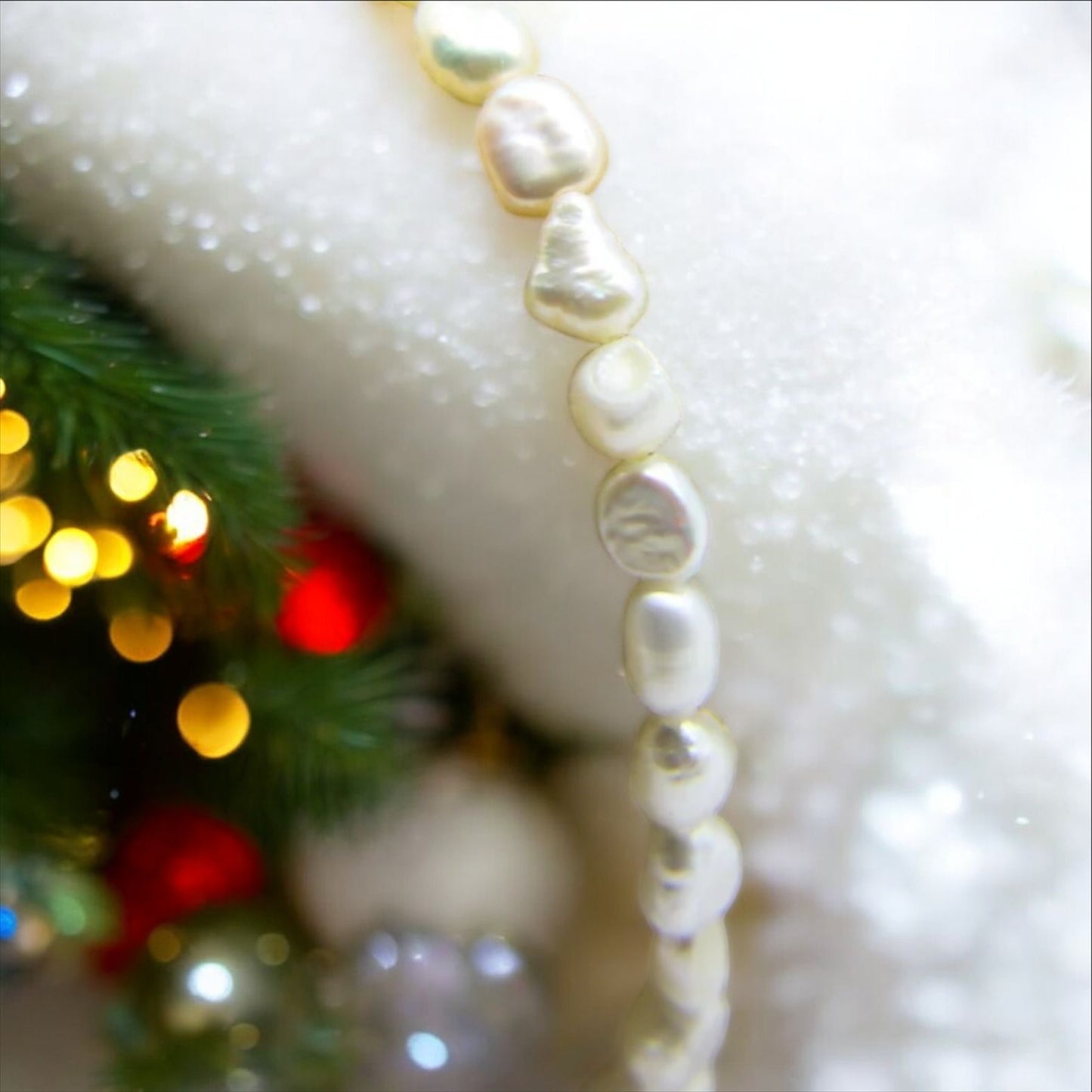 Pearl bracelet on snow with Christmas decorations.  