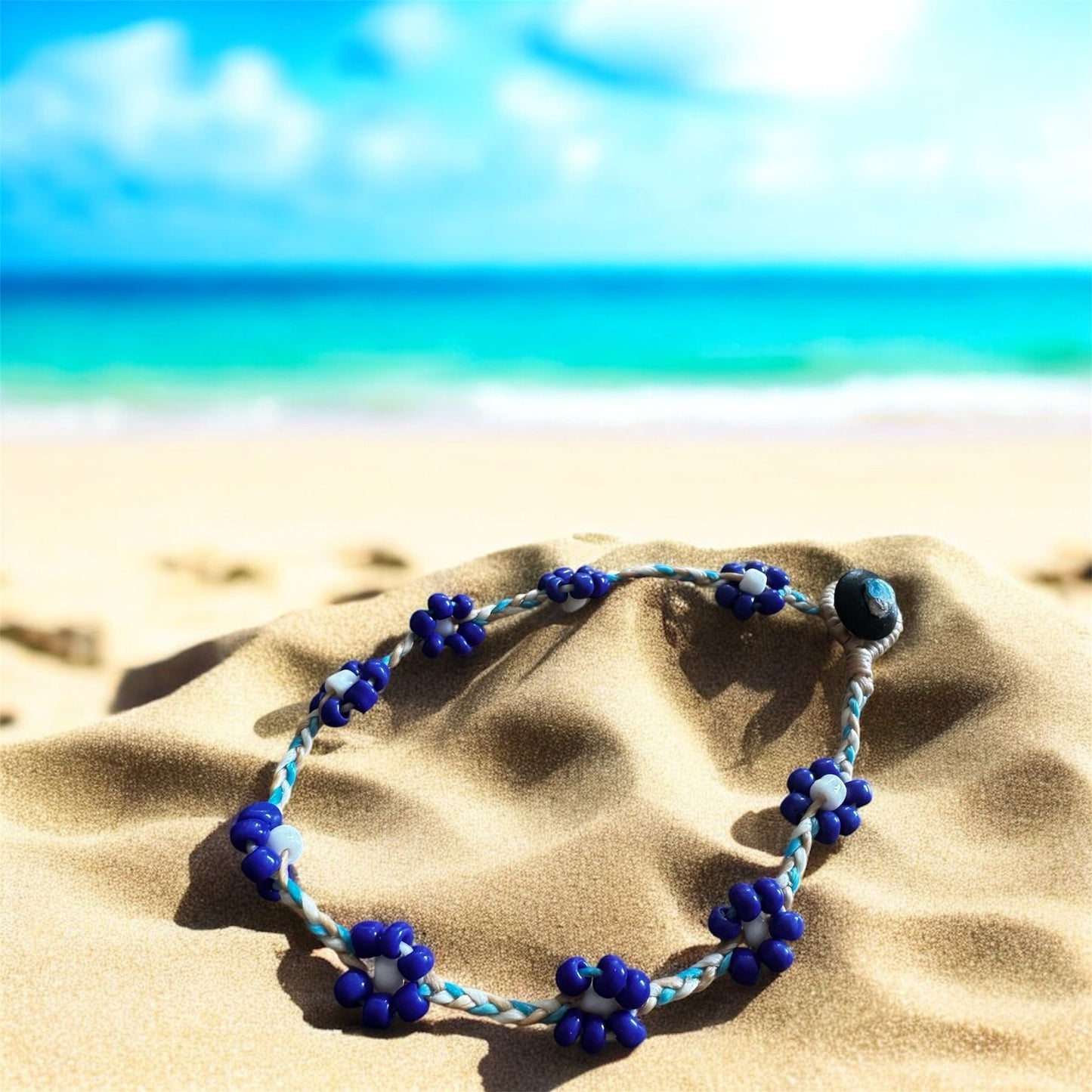 String anklet with beads in a flower design. Anklet is on a beach with the sea behind. 