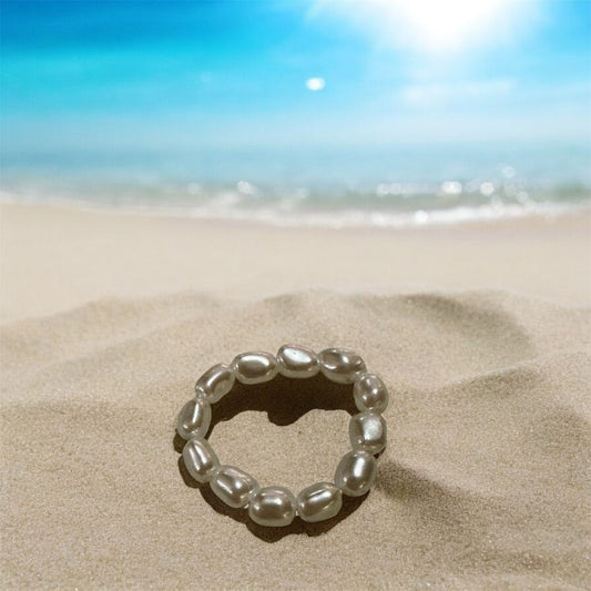 Pearl stretch ring on a beach with bright sun and blue sea behind. 