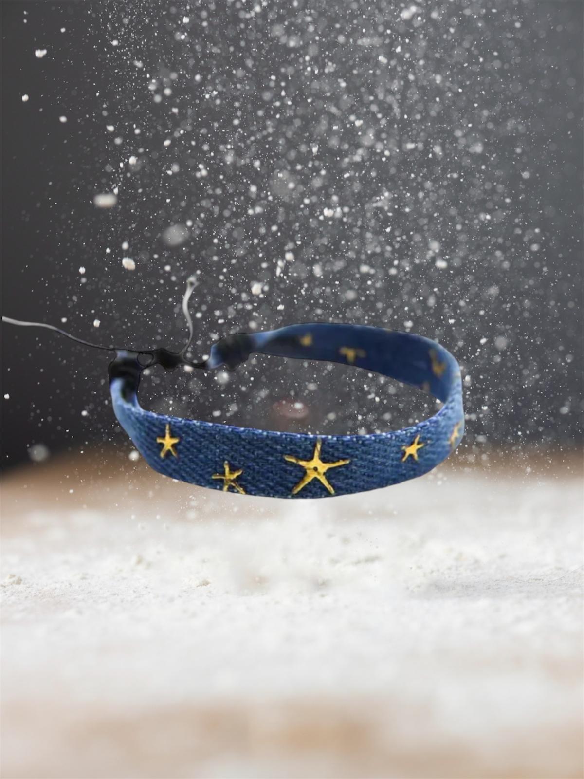 Blue denim bracelet with gold star motifs floating in a snow storm. 