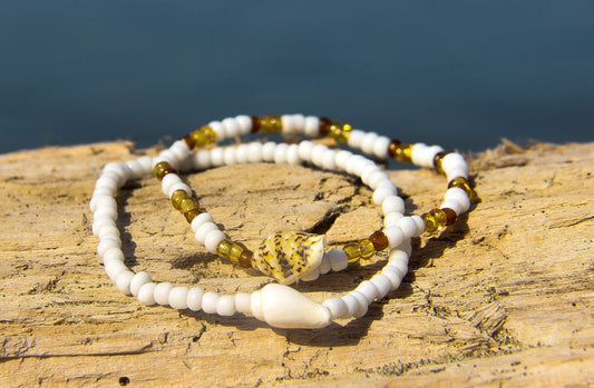 Close-up of 2 white and amber beaded bracelets on drift-wood in front of sea