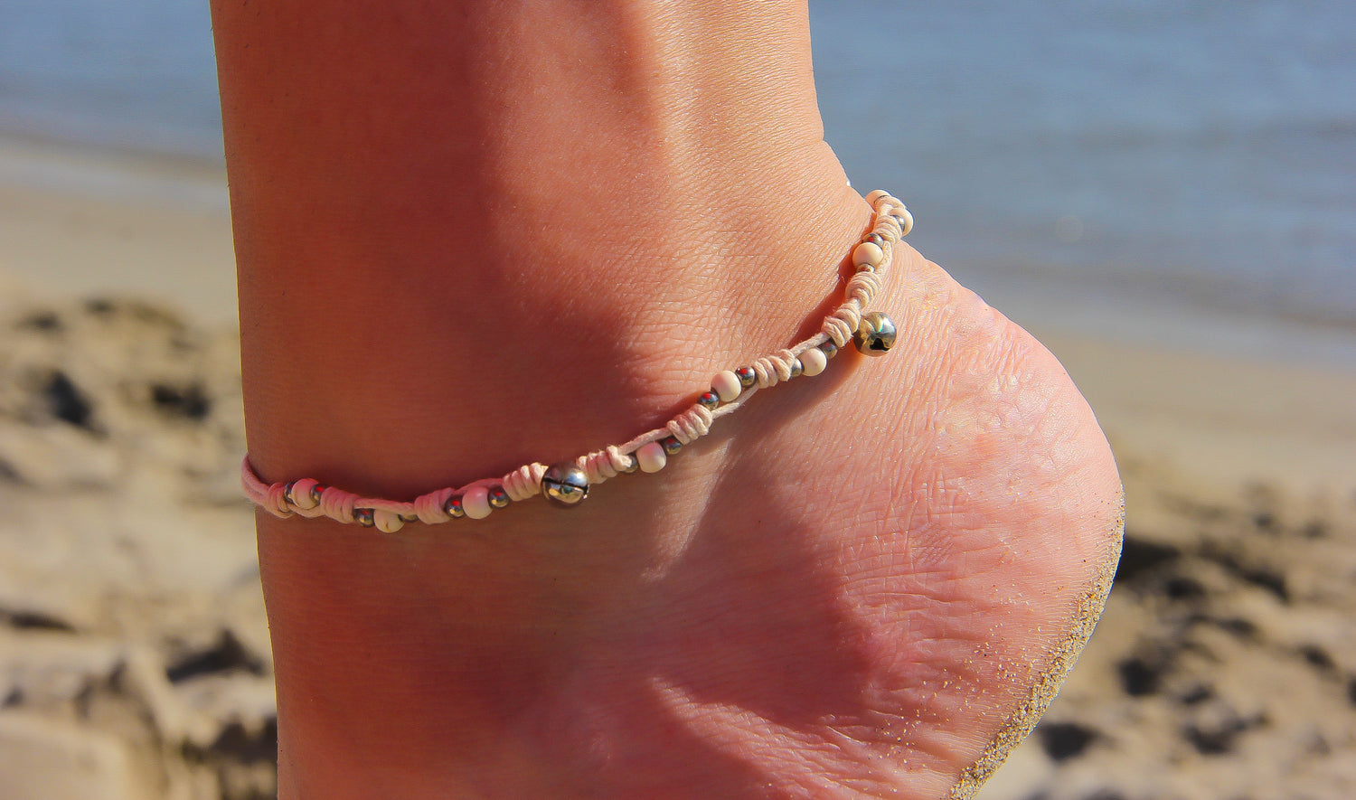 Close-up of anklet with bells | Beach and sea in background