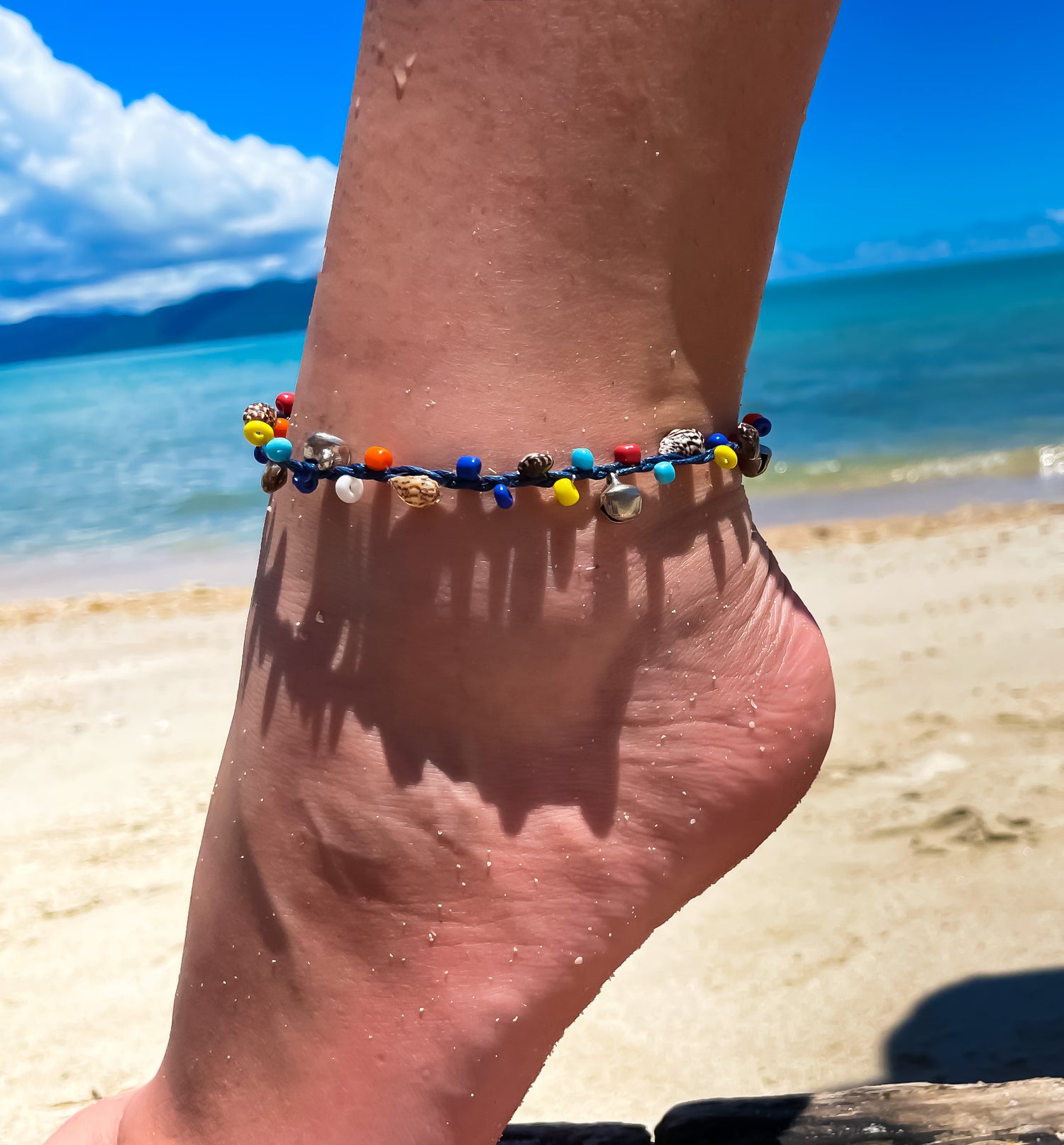 model wearing beaded anklet with sea behind. 