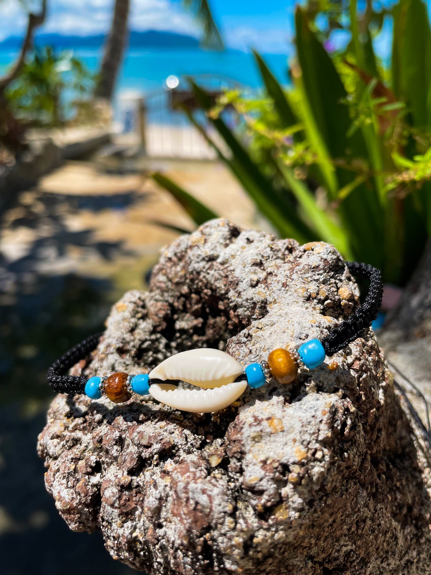 Necklace with cowrie shell and beads displayed on rock with beach and sea behind