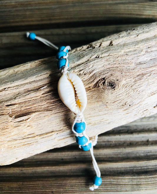 Beach Bracelet wrapped around a piece of driftwood. Bracelet is made of braised cream string with blue stone beads and a cowrie shell.