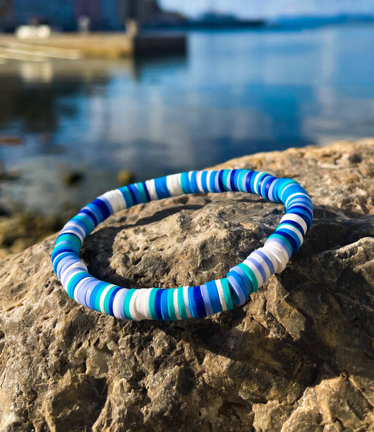 blue and white stripped beach bracelet on a rock with the sea behind. 