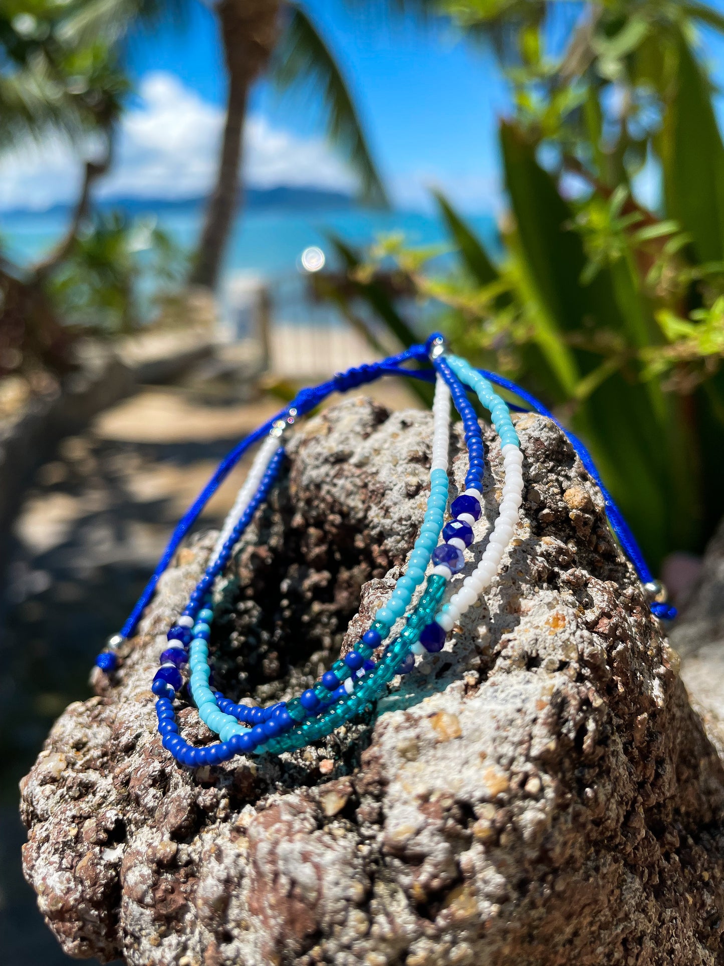 Blue, white and turquoise beaded bracelet on a rock and beach and sea behind. 