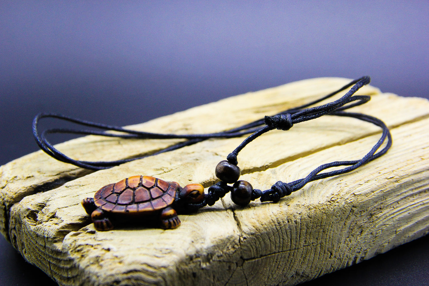 Necklace with brown sea turtle pendant on a piece of wood. 