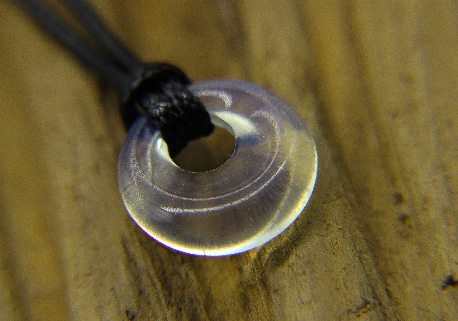 Clear quartz pendant on a black cord choker on a piece of wood. 