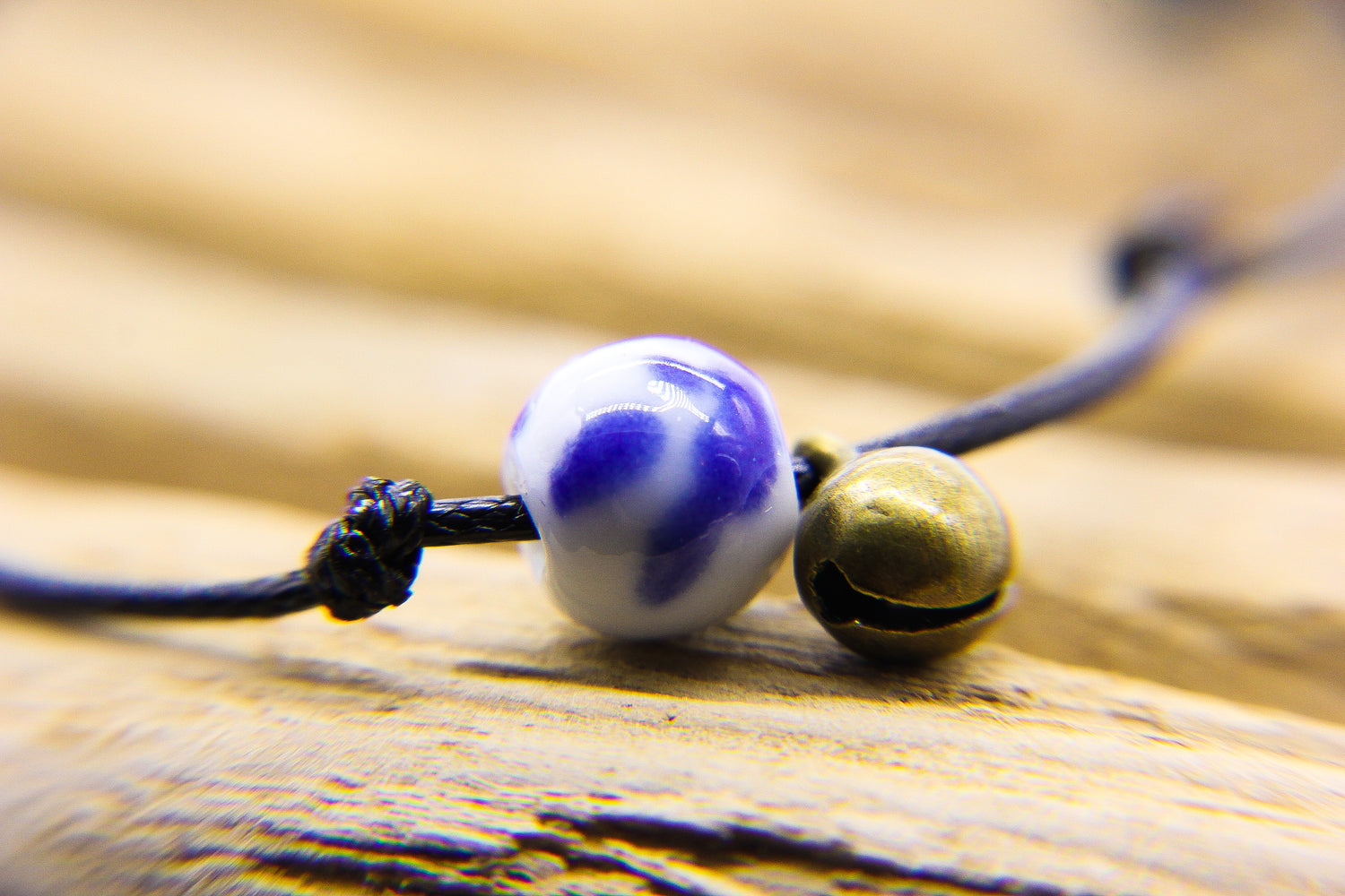Close up a blue and white delft-style porcelain bead and brass bell on a black cord. 