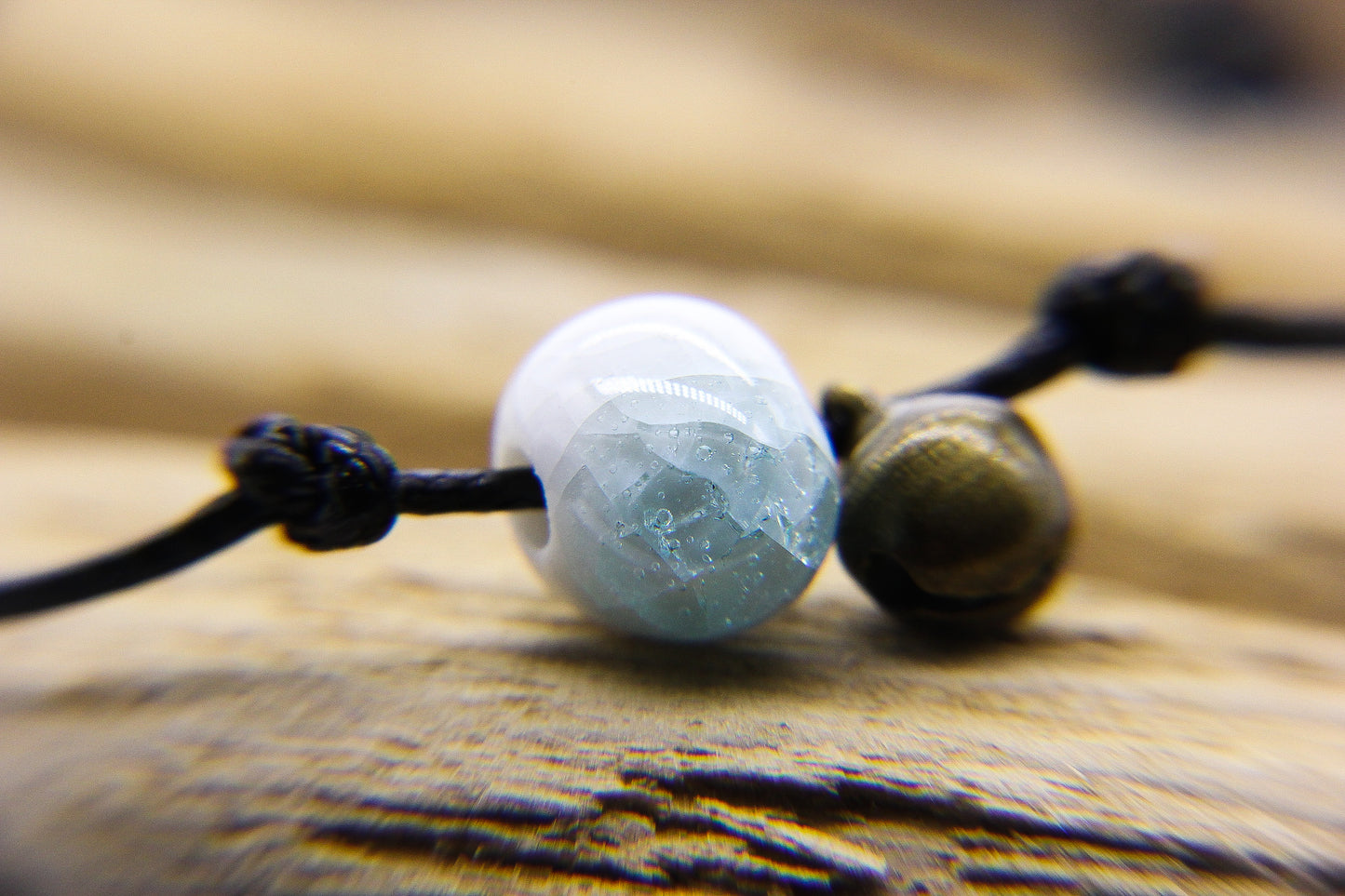 Close up of blue and white glass bead and brass bell on a black cord bracelet 