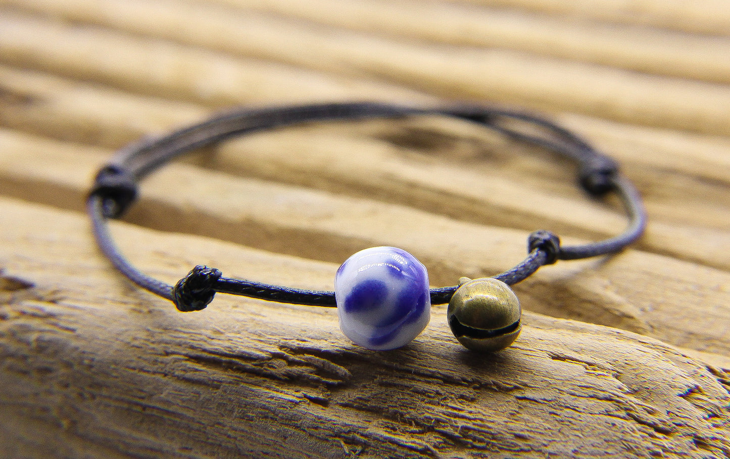 Bracelet of black waxed cord with tiny brass bell and blue and white china bead 