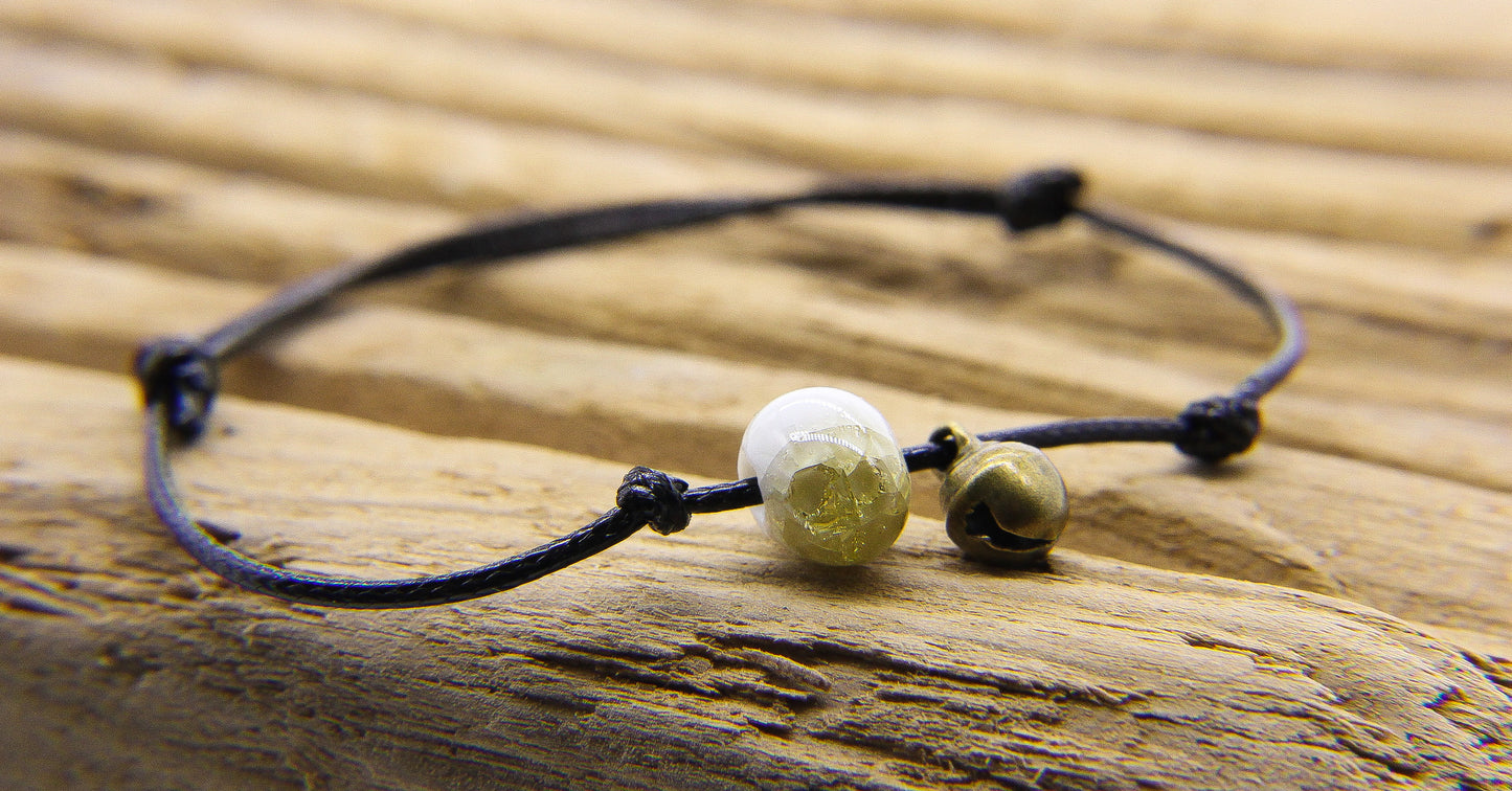 Black cord bracelet with yellow and white glass bead and tiny brass bell. 