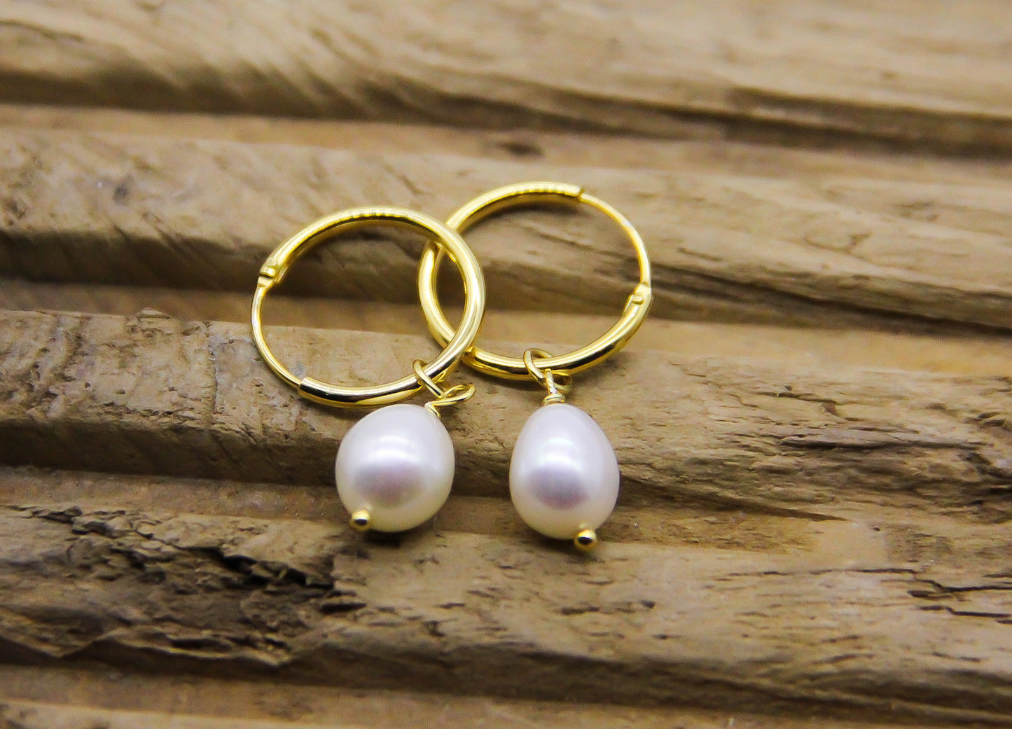 gold huggie hoop pearl drop earrings on a piece of driftwood