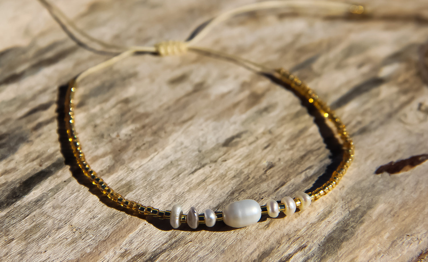Gold seed bead bracelet with pearls displayed on a piece of driftwood 