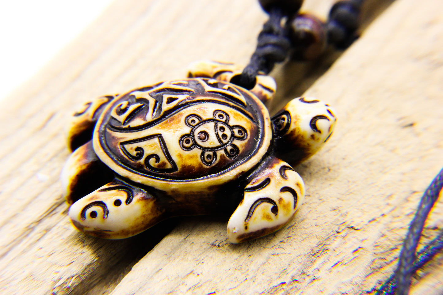 Close-up of carved sea turtle pendant on black necklace | Pendant is on a piece of wood