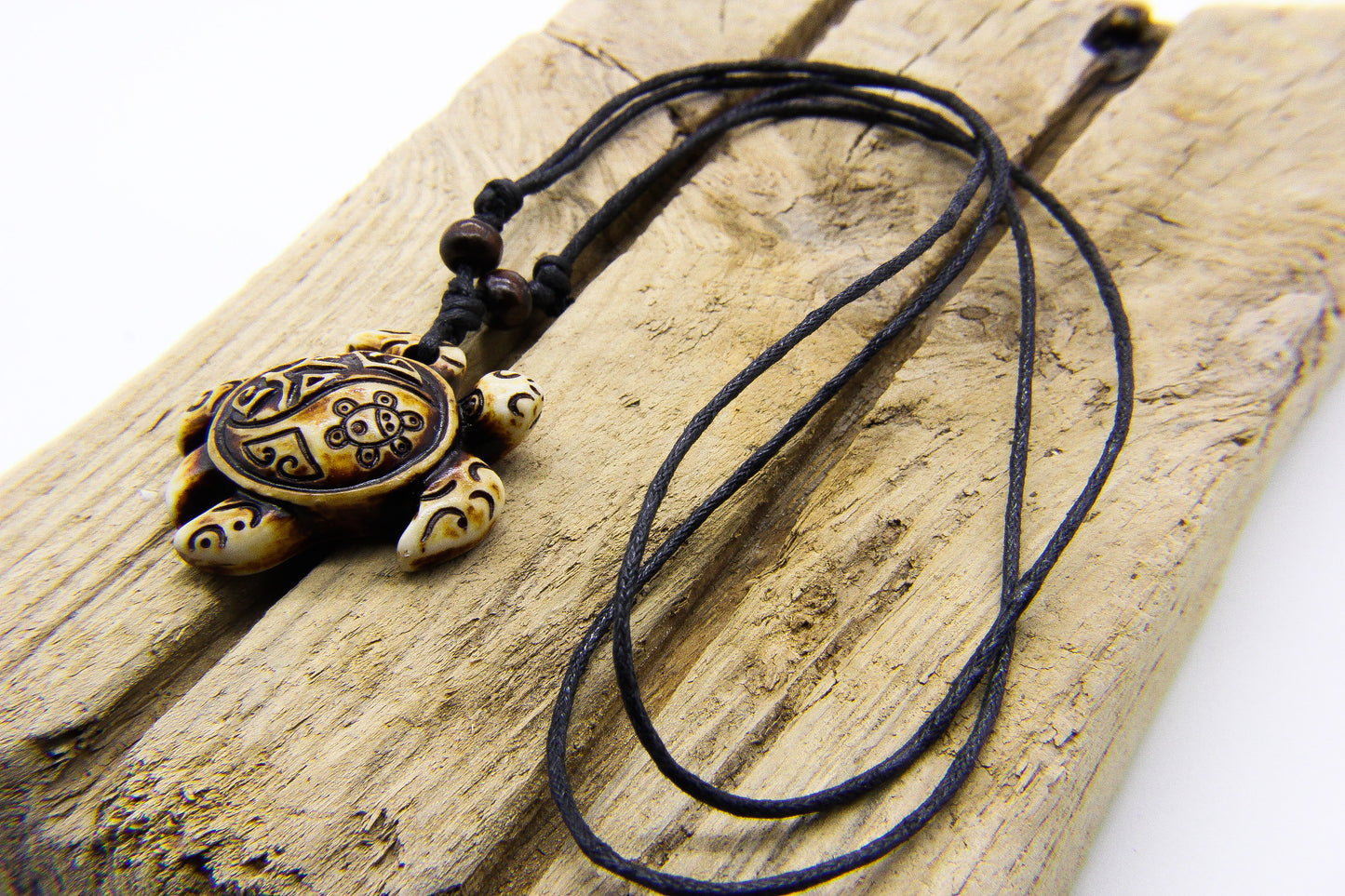 Black cord necklace with decorative sea turtle pendant on a piece of slatted wood