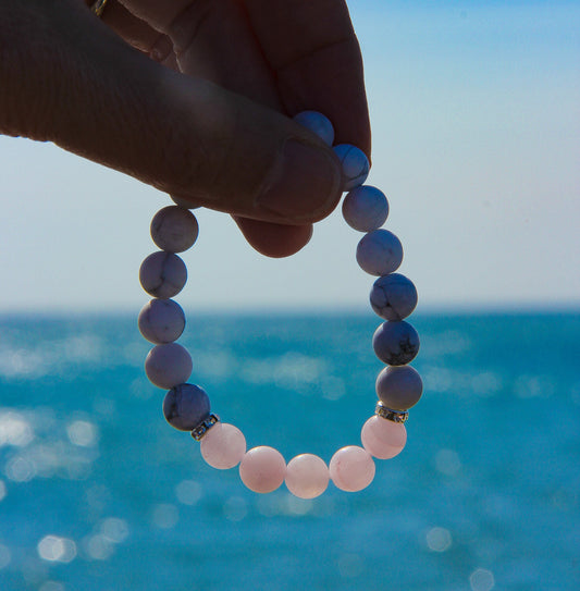Model's hand holding a beaded bracelet with the sea in the background