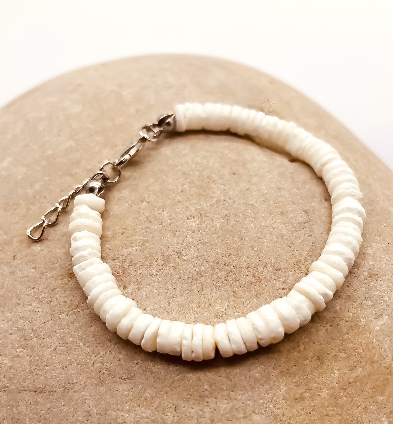 white shell bracelet with silver catch displayed on a pebble