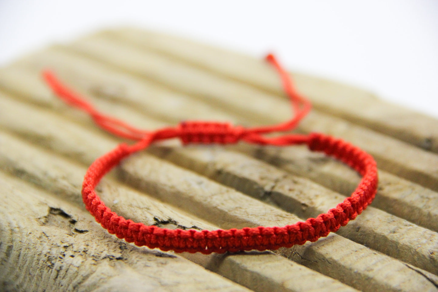 red friendship bracelet displayed on driftwood