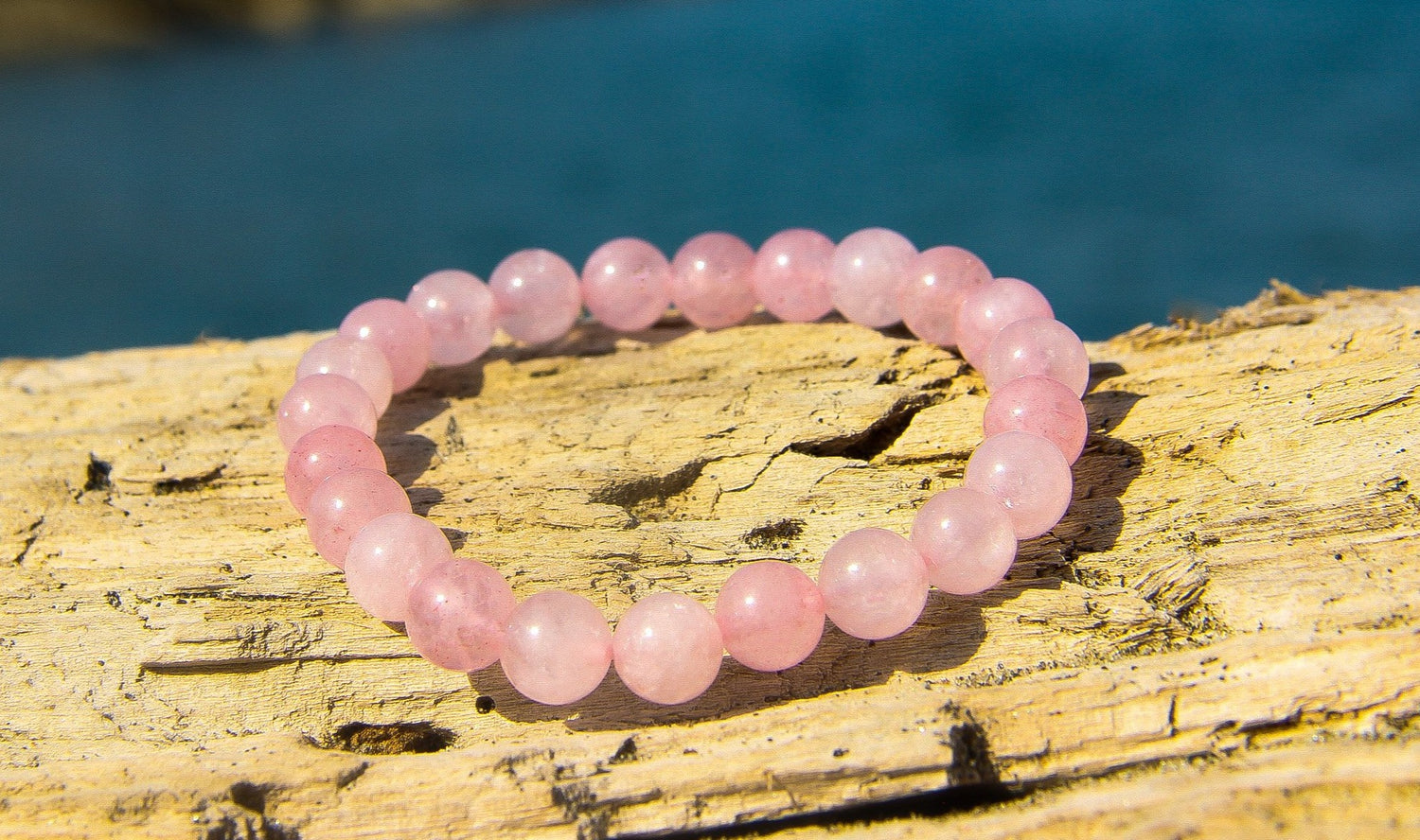 Rose Quartz Beaded Bracelet on a piece of driftwood with the sea behind
