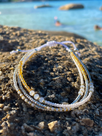 gold and white seed bead anklet on a rock with sea behind