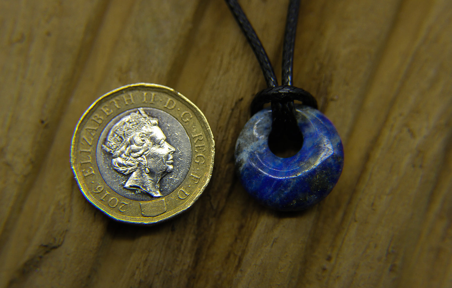 Circular gemstone pendant on a black choker with pound coin to compare size 