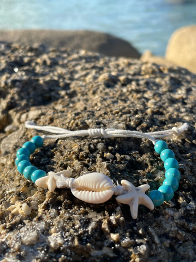 Beach bracelet of turquoise beads and shells on a rock with the sea behind