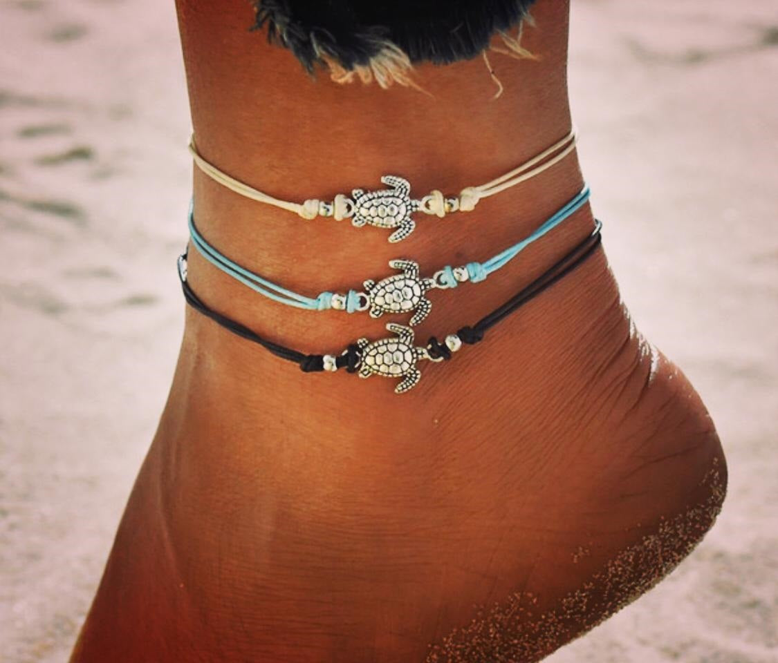 Model's ankle with 3 anklets in black, cream and blue each with a silver sea turtle pendant