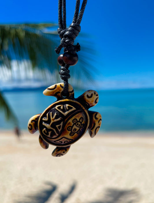 Necklace with carved sea turtle pendant , beach and sea behind, Bens Beach Jewellery UK