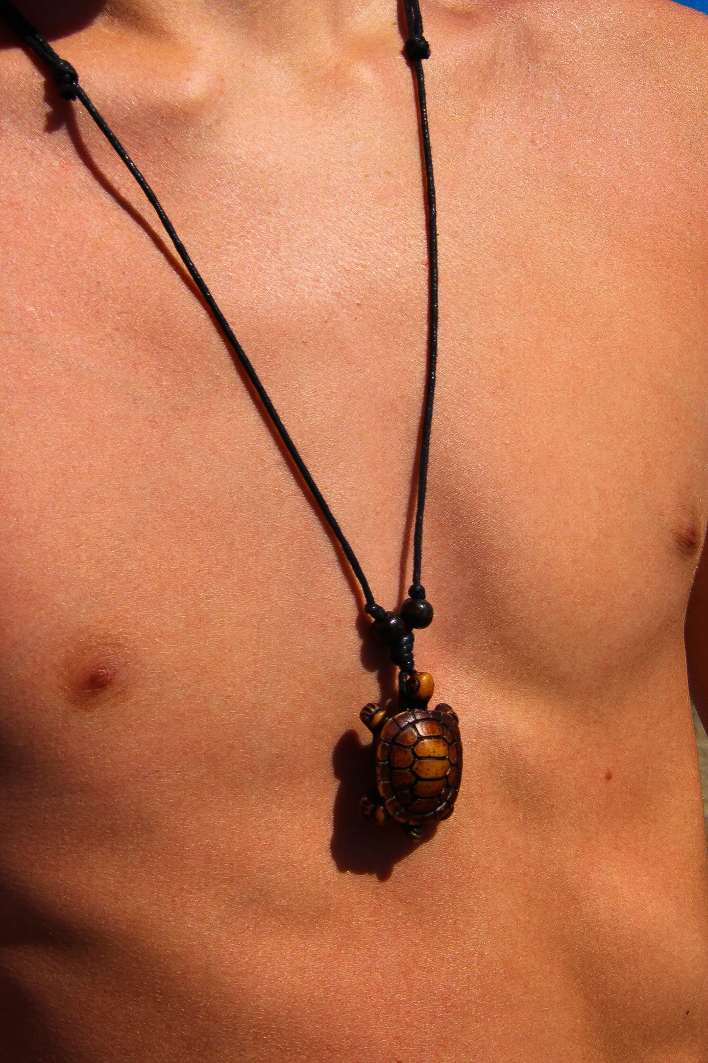 Male model with bare chest wearing a black necklace with carved sea turtle choker