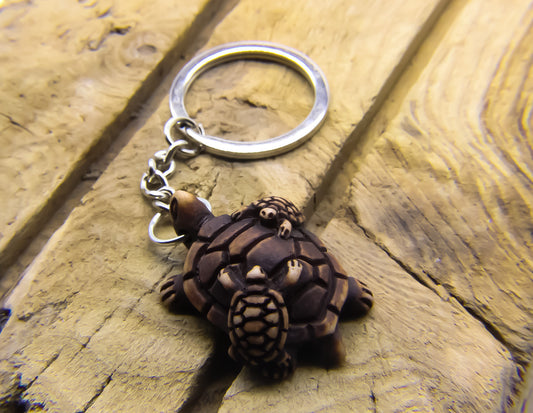 Keyring with adult and children sea turtle pendant and stainless steel keychain. Key ring is on a piece of slatted wood. 