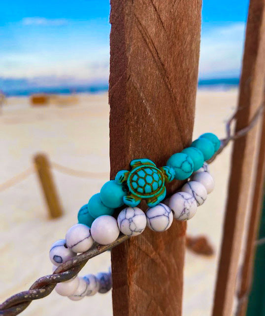 Stone bracelets wrapped around a fence post at the beach. Turquoise bracelet has sea turtle charm