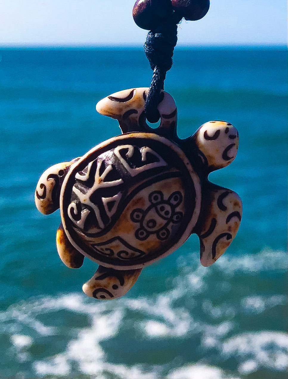 Close-up of carved sea turtle pendant with sea in background
